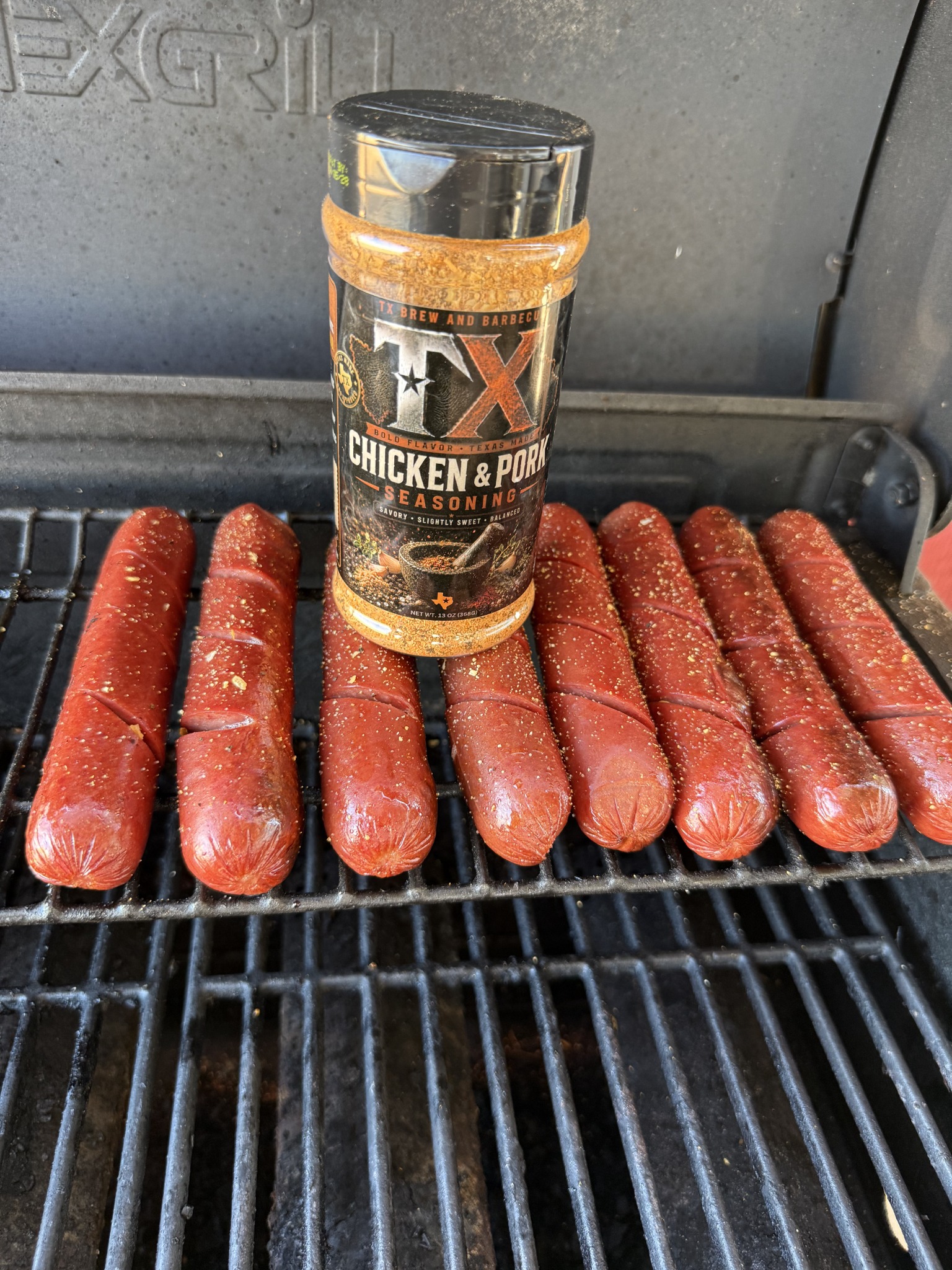 Chicken and Pork seasoning bottle with hotdogs on a grill
