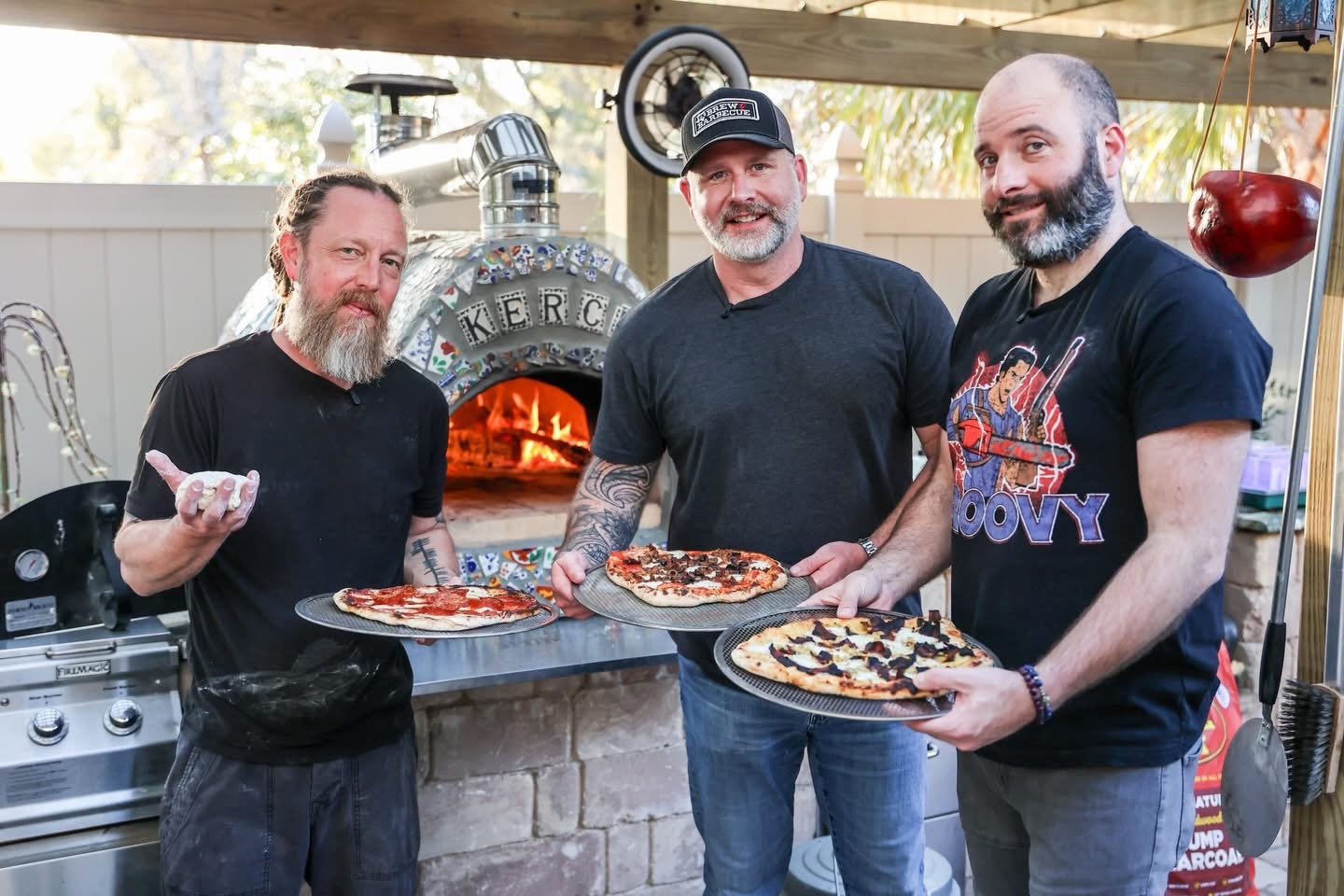 Ty Sherrell and friends holding pizzas in front of a wood-fired oven