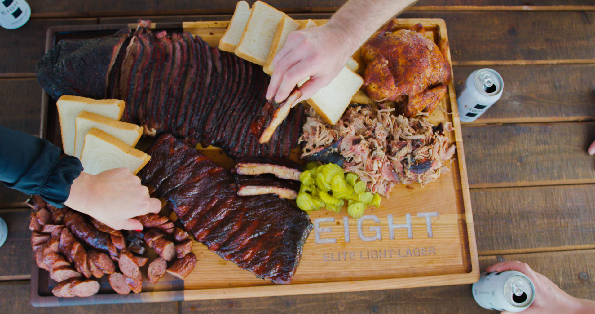 Overhead shot of a full barbecue board: brisket, ribs, pulled pork, sausage, chicken and fixings